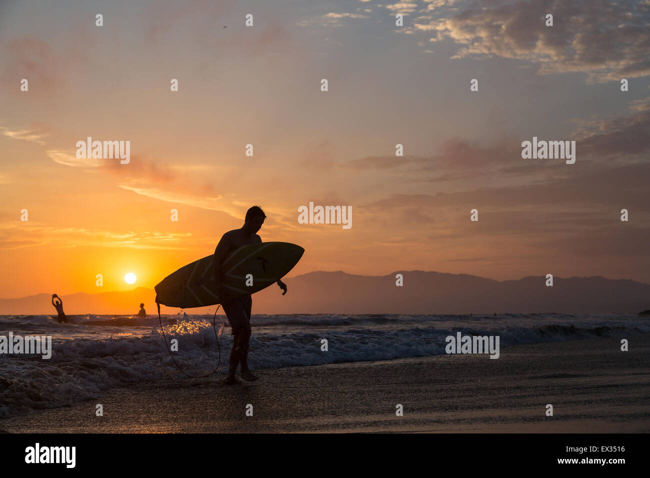 Un surfista esce l'acqua a Venezia spiaggia al tramonto. Foto Stock