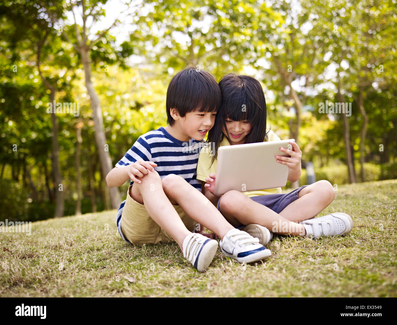 Ragazza asiatica e ragazzo giocare con l'ipad all'aperto nel parco. Foto Stock