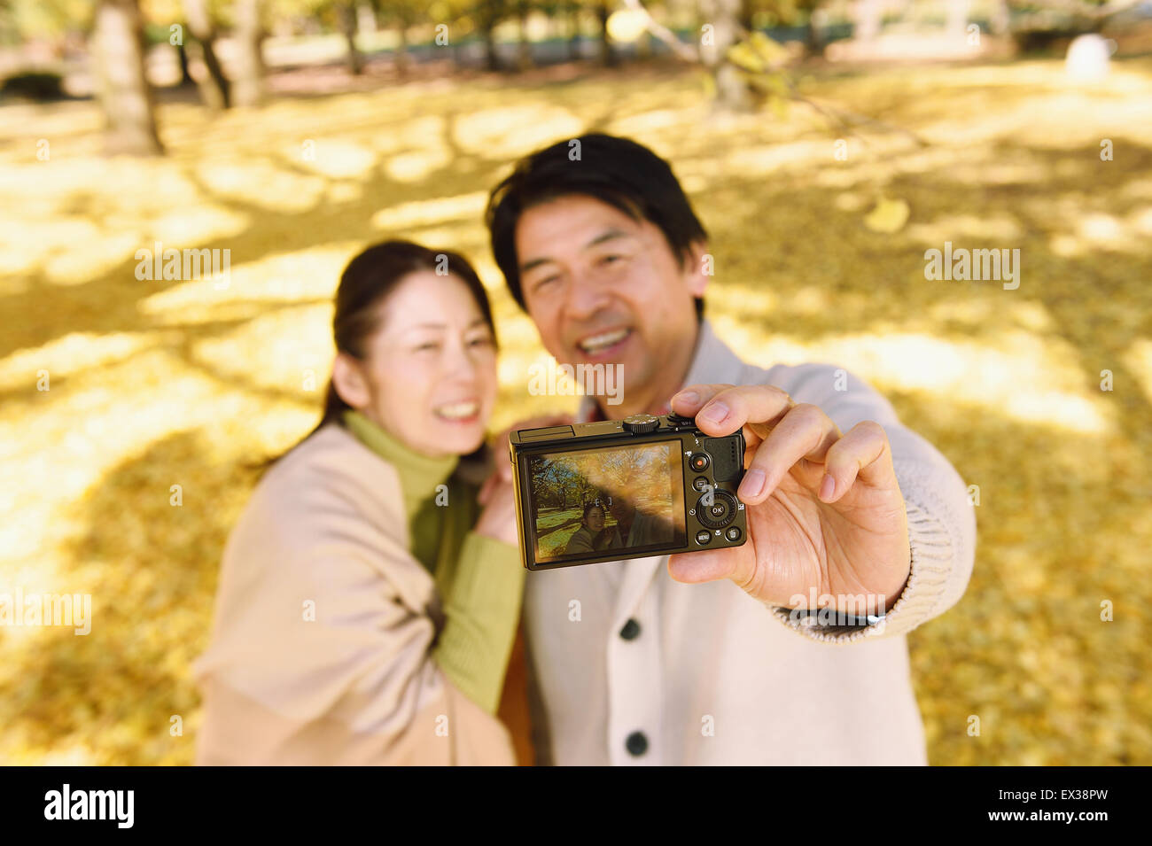 Senior coppia giapponese a scattare foto in un parco della città in autunno Foto Stock