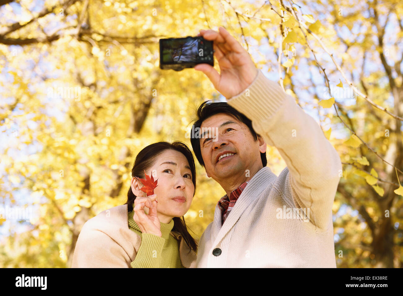 Senior coppia giapponese a scattare foto in un parco della città in autunno Foto Stock