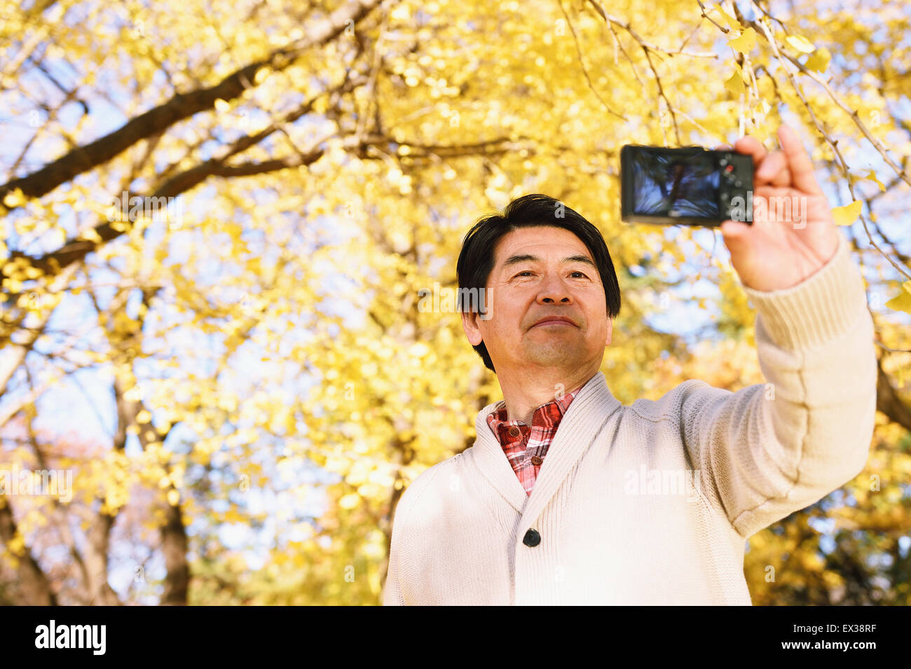 Senior uomo giapponese prendendo un selfie in un parco della città in autunno Foto Stock