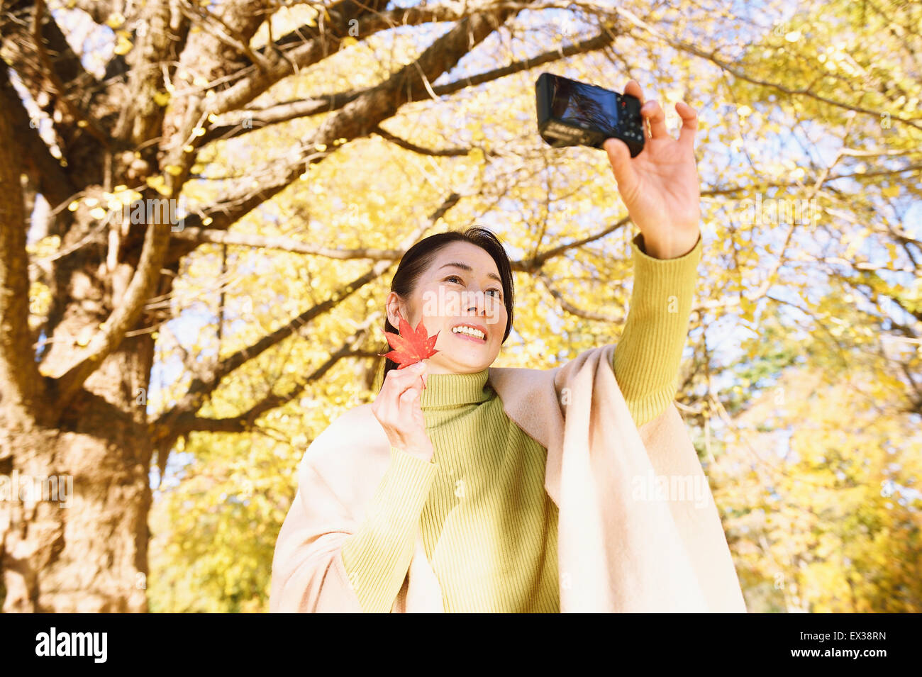 Senior donna giapponese prendendo un selfie in un parco della città in autunno Foto Stock