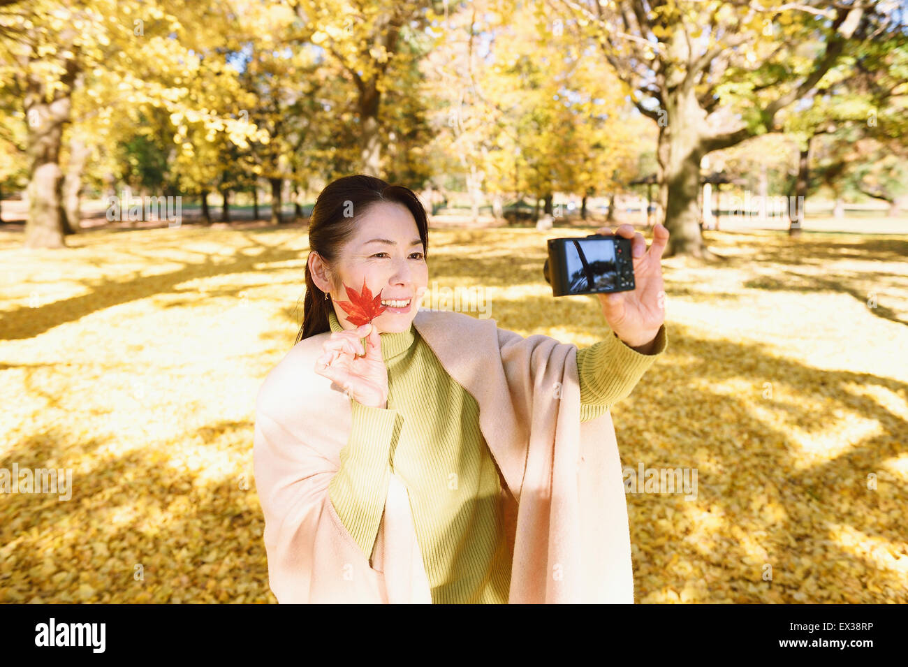 Senior donna giapponese prendendo un selfie in un parco della città in autunno Foto Stock
