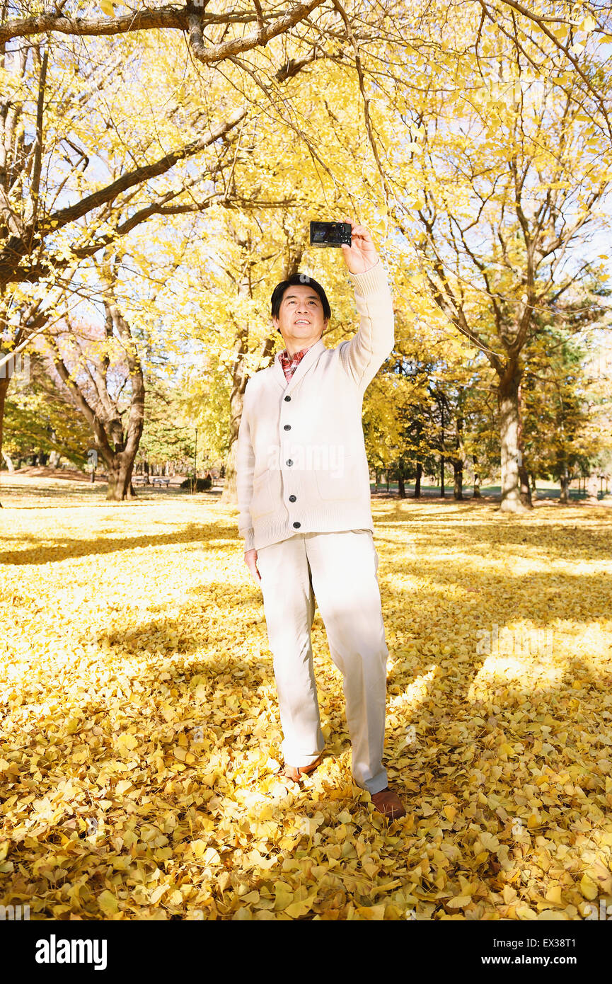 Senior uomo giapponese prendendo un selfie in un parco della città in autunno Foto Stock
