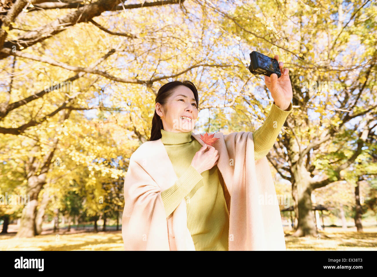 Senior donna giapponese prendendo un selfie in un parco della città in autunno Foto Stock