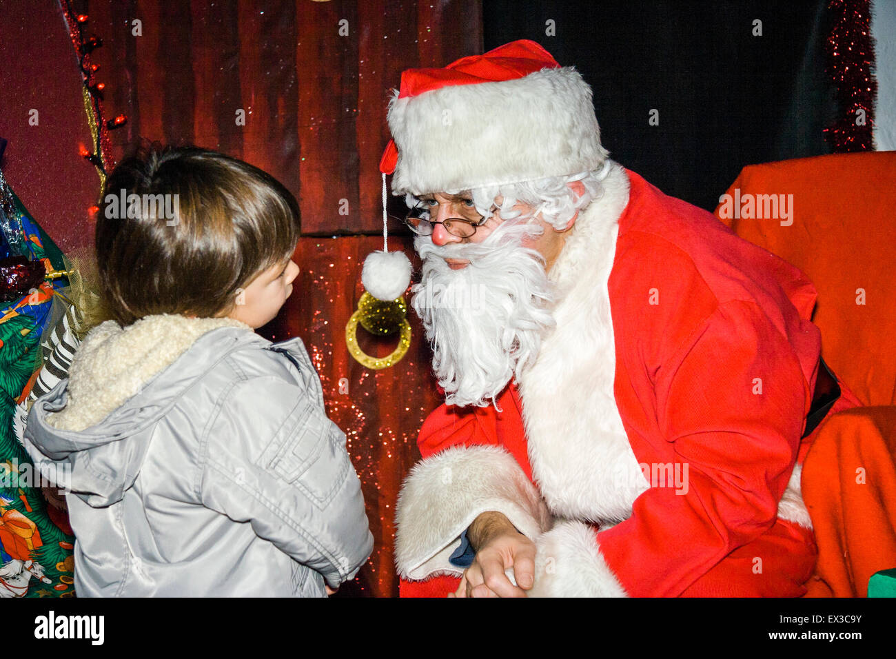 Ragazzo in Santa Grotta di essere interrogato da Babbo Natale. Bambino caucasico, 3-4 anni, indossa cappotto invernale Santa circondato da presenta. Foto Stock