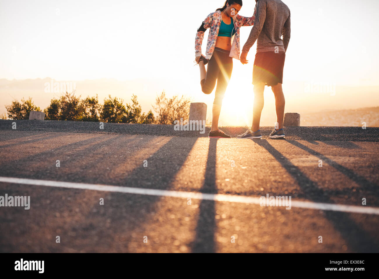 Colpo all'aperto di giovani praticanti di jogging stretching prima di una corsa la mattina. Giovane uomo e donna stretching le gambe a sunrise. Foto Stock