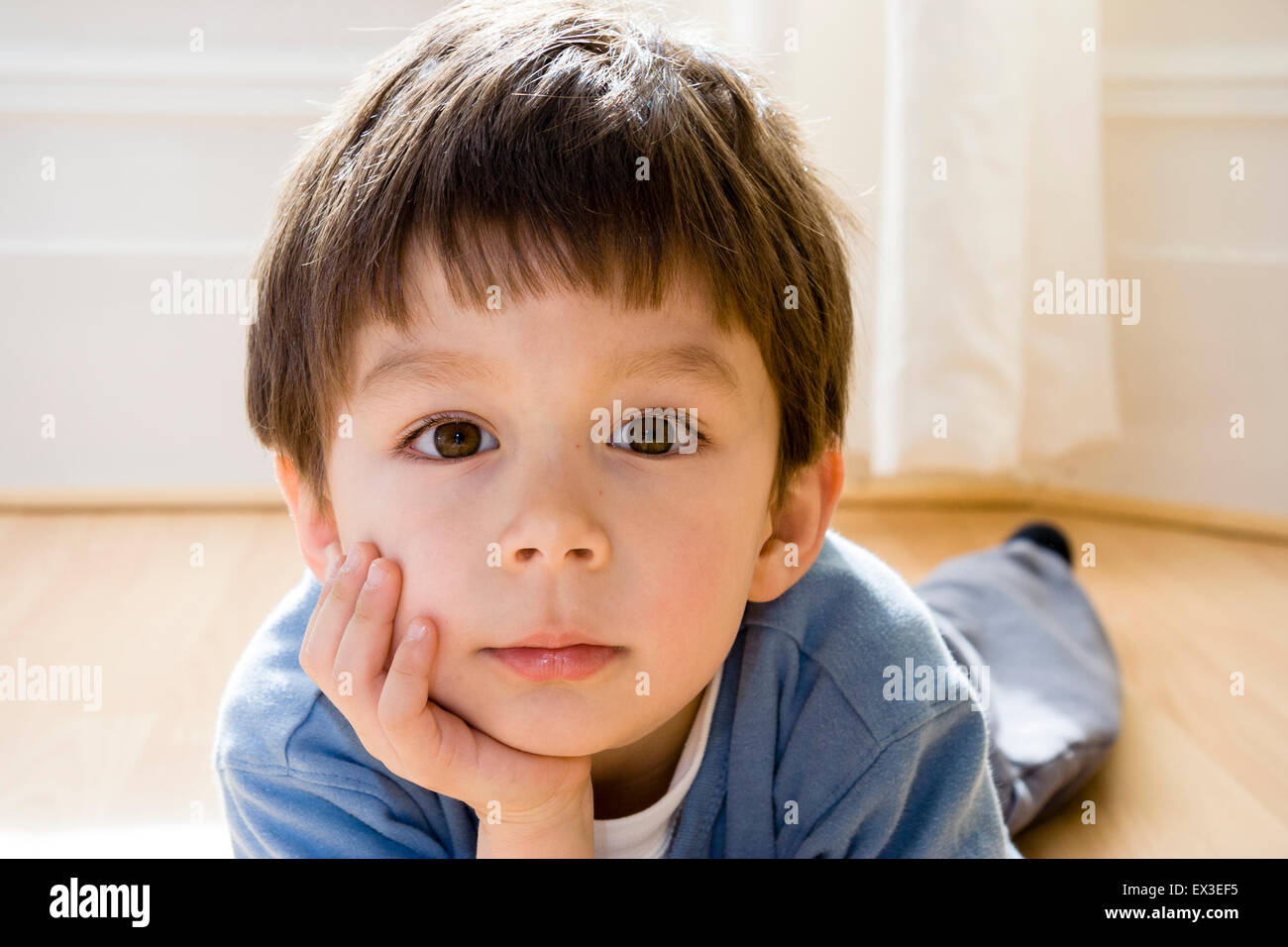 Bambino caucasico, boy, 5-6 anni, ibndoors posa su pavimento di legno sul lato di appoggio della faccia a portata di mano e guardando direttamente al visualizzatore. Foto Stock