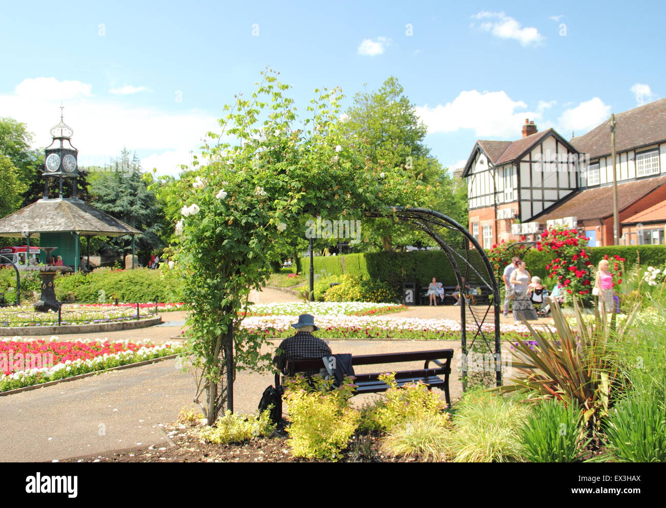 Un uomo si siede su una panchina sotto un arco di rose in una calda giornata estiva in Hall Leys Park, Matlock, Derbyshire Dales, England Regno Unito Foto Stock