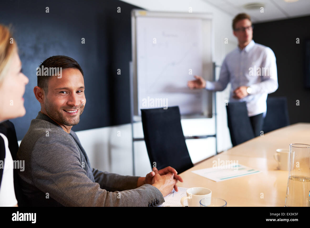 I giovani maschi bianchi sorride esecutivo e di fronte alla fotocamera durante la riunione di lavoro Foto Stock