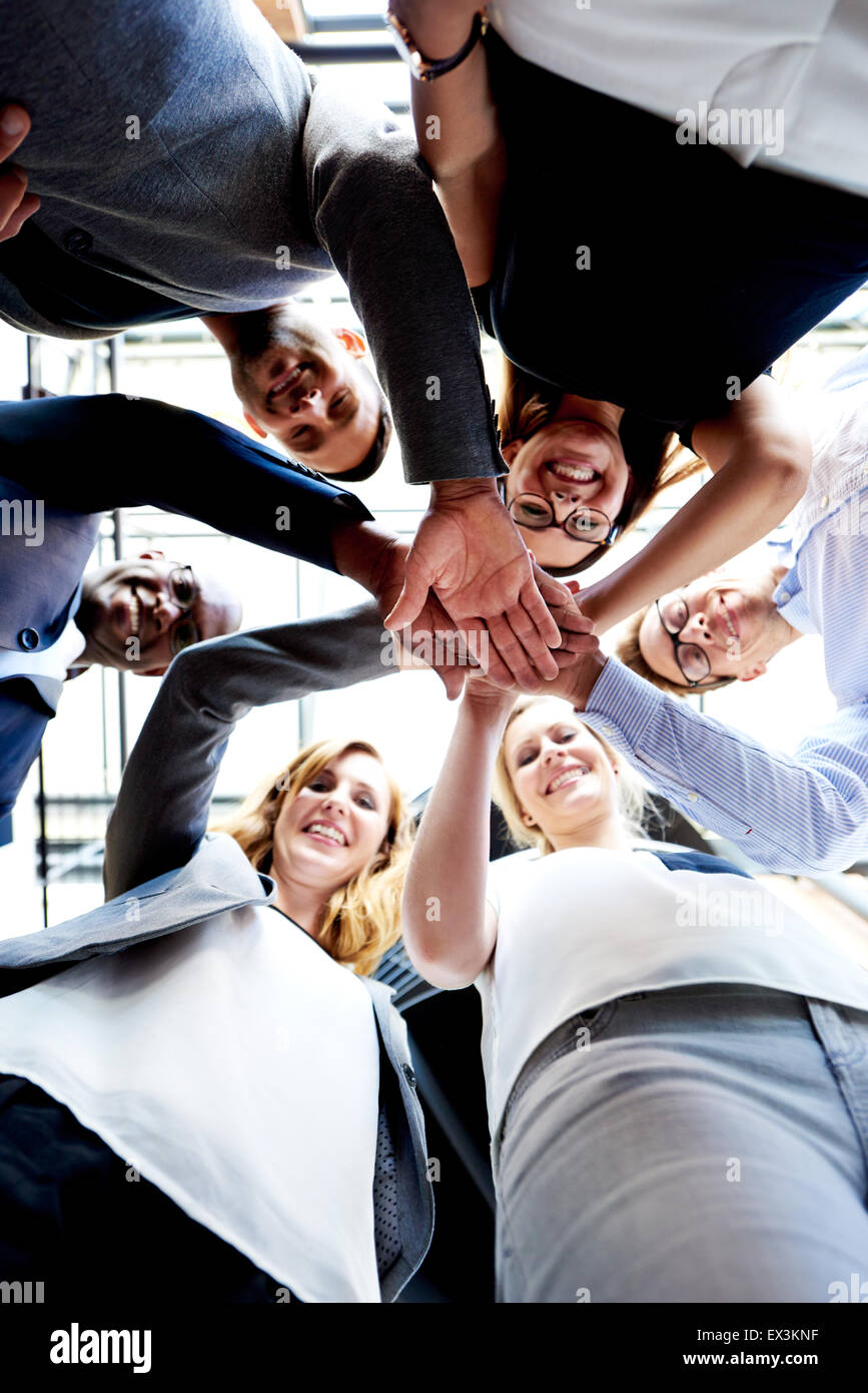 Collaboratori in piedi in cerchio le mani insieme guardando giù in telecamera Foto Stock