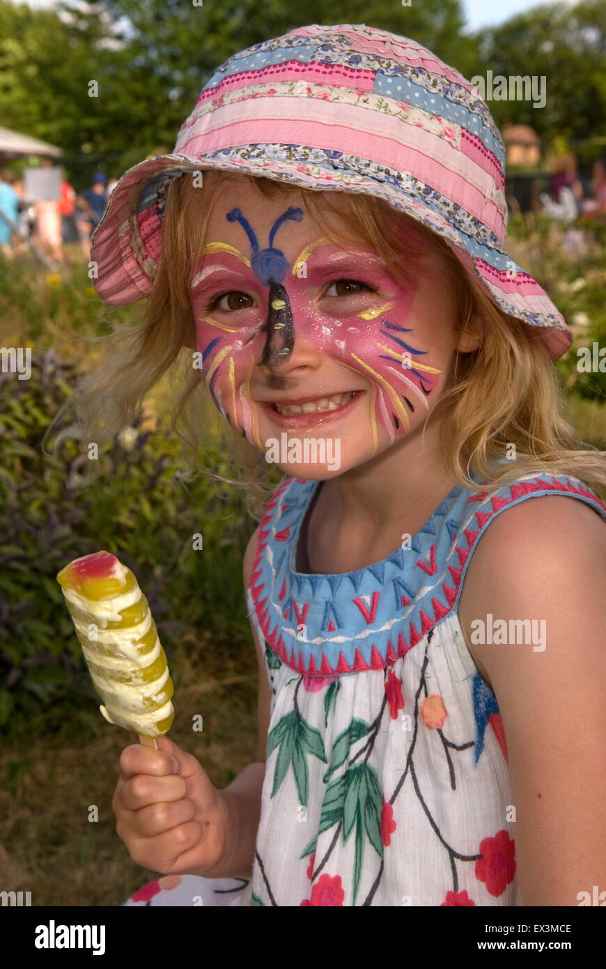 Un felice, smiley 3 anno vecchia ragazza con la faccia dipinta e per lecca-lecca di ghiaccio in una scuola estiva, equo Headley, Hampshire, Regno Unito. Foto Stock