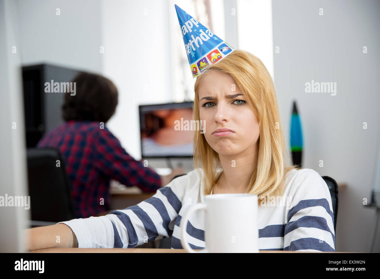 Triste donna con cappello compleanno seduti a tavola in ufficio e guardando  la fotocamera Foto stock - Alamy