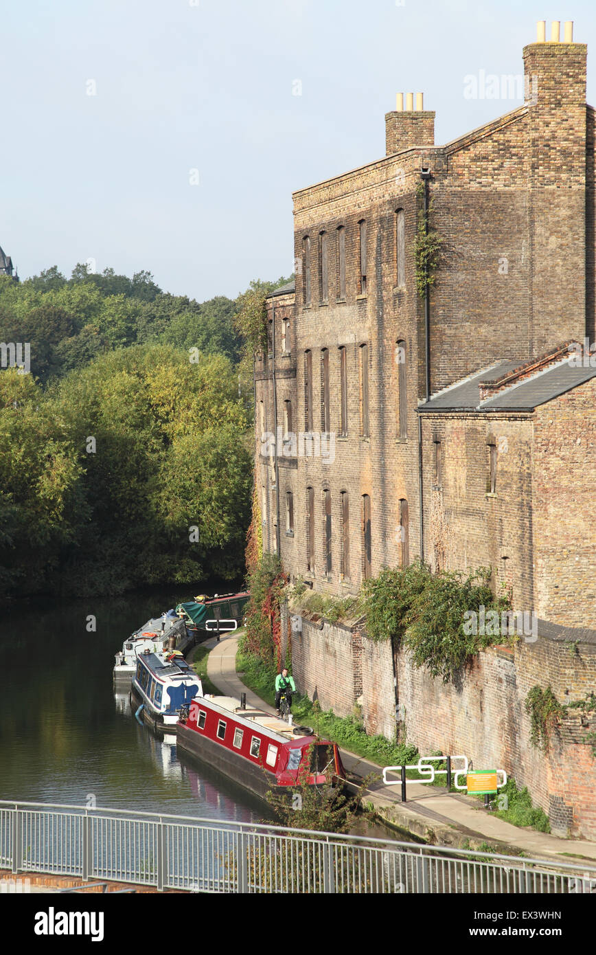 Un ciclista passa ormeggiate imbarcazioni strette e gli edifici in stile vittoriano sul Regents Canal vicino a Kings Cross nel centro di Londra Foto Stock