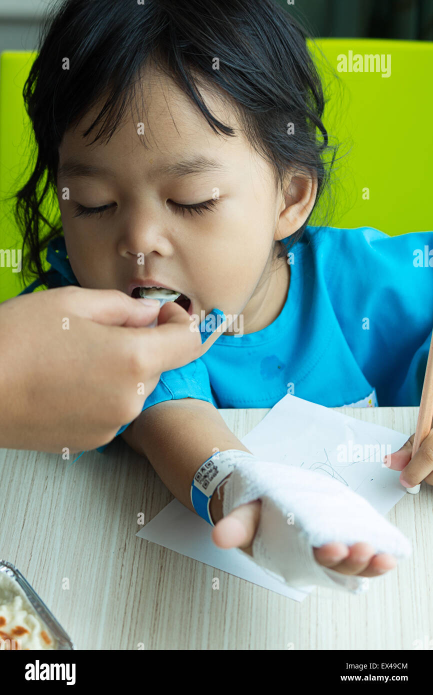 Malattia bambini asiatici carta da scrivere sulla scrivania e mangiare cereali, soluzione salina per via intravenosa (IV) a portata di mano Foto Stock