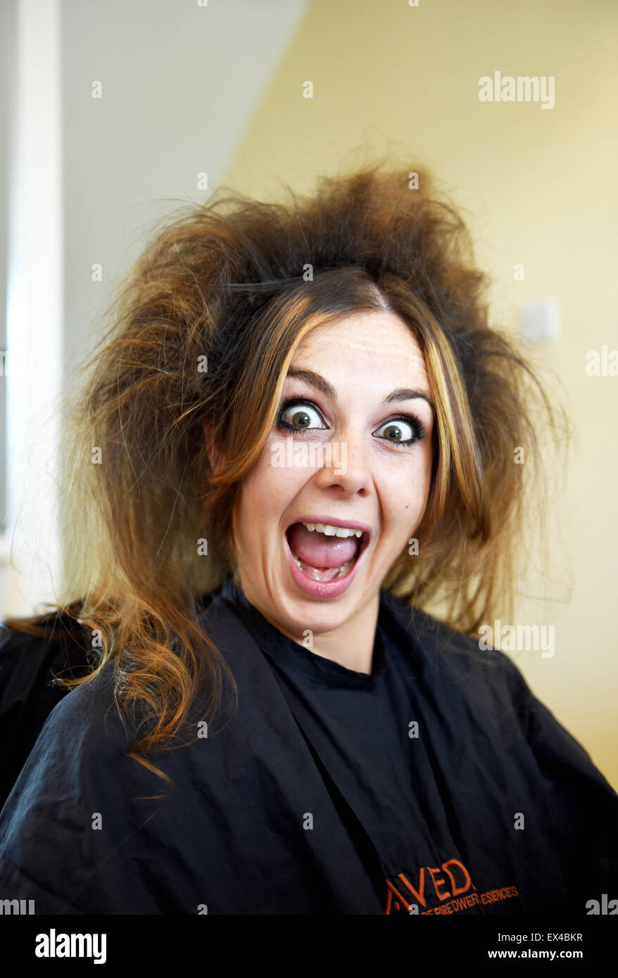 Giovane sposa avente il suo matrimonio capelli preparati da parrucchiere a casa la mattina del grande giorno utilizzando indietro tecnica di pettinatura Foto Stock