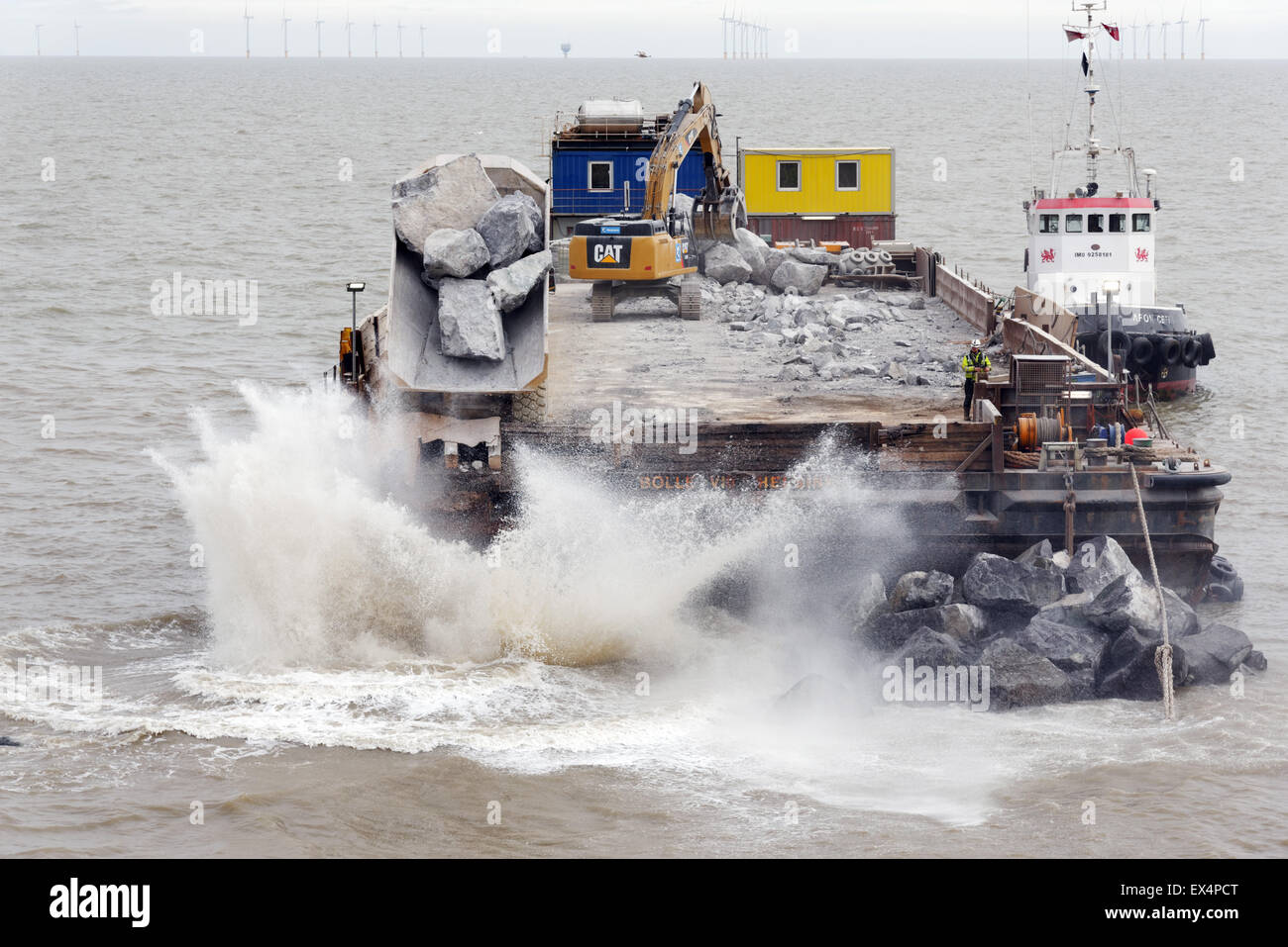 Una chiatta essendo utilizzato per rendere le difese del mare - un dumping camion enormi massi in mare per rendere un frangiflutti. Clacton-on-Sea Essex Foto Stock