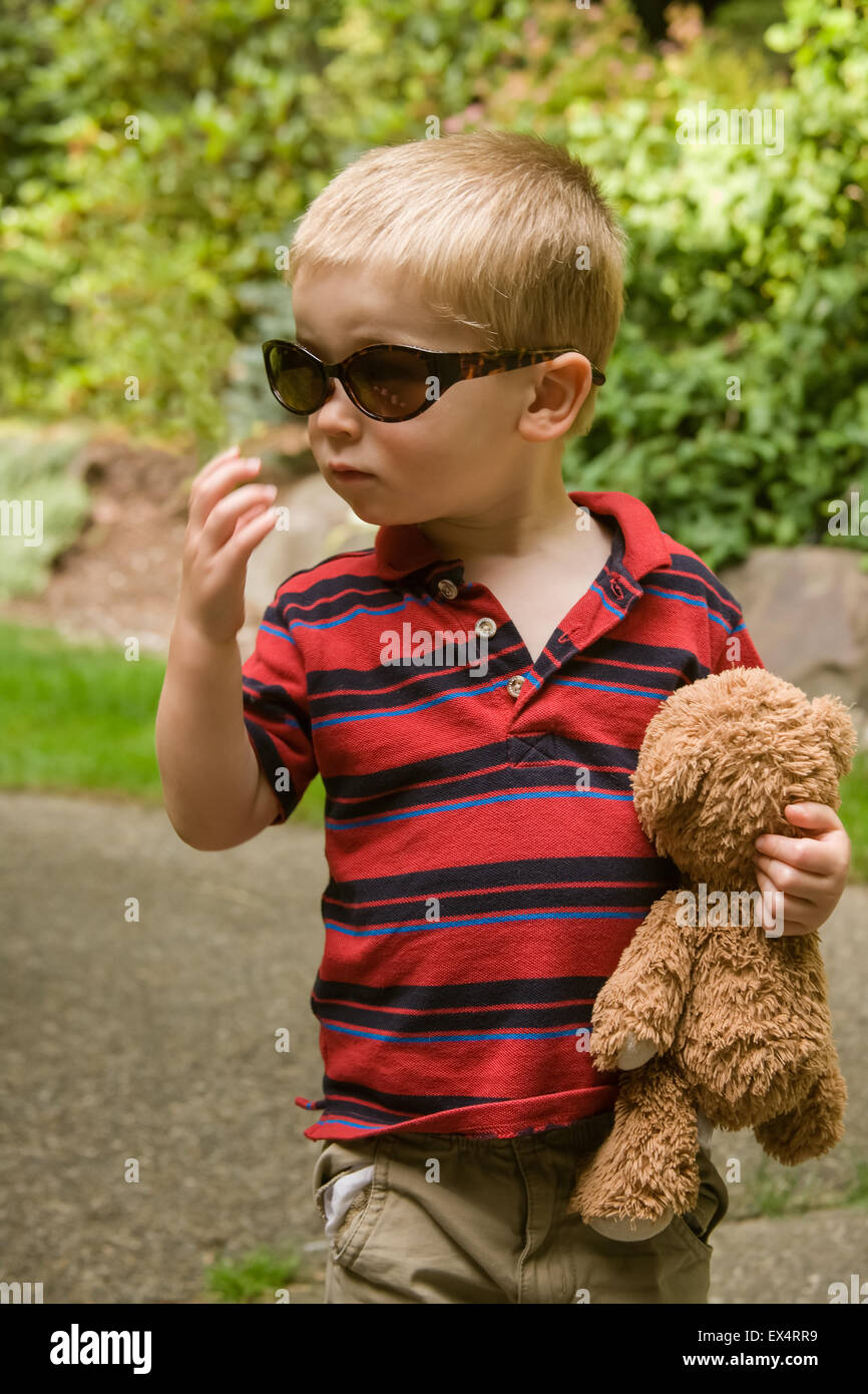 Bimbo di 2 anni che porta un orsacchiotto di peluche e indossando askew  Mom's occhiali da sole Foto stock - Alamy