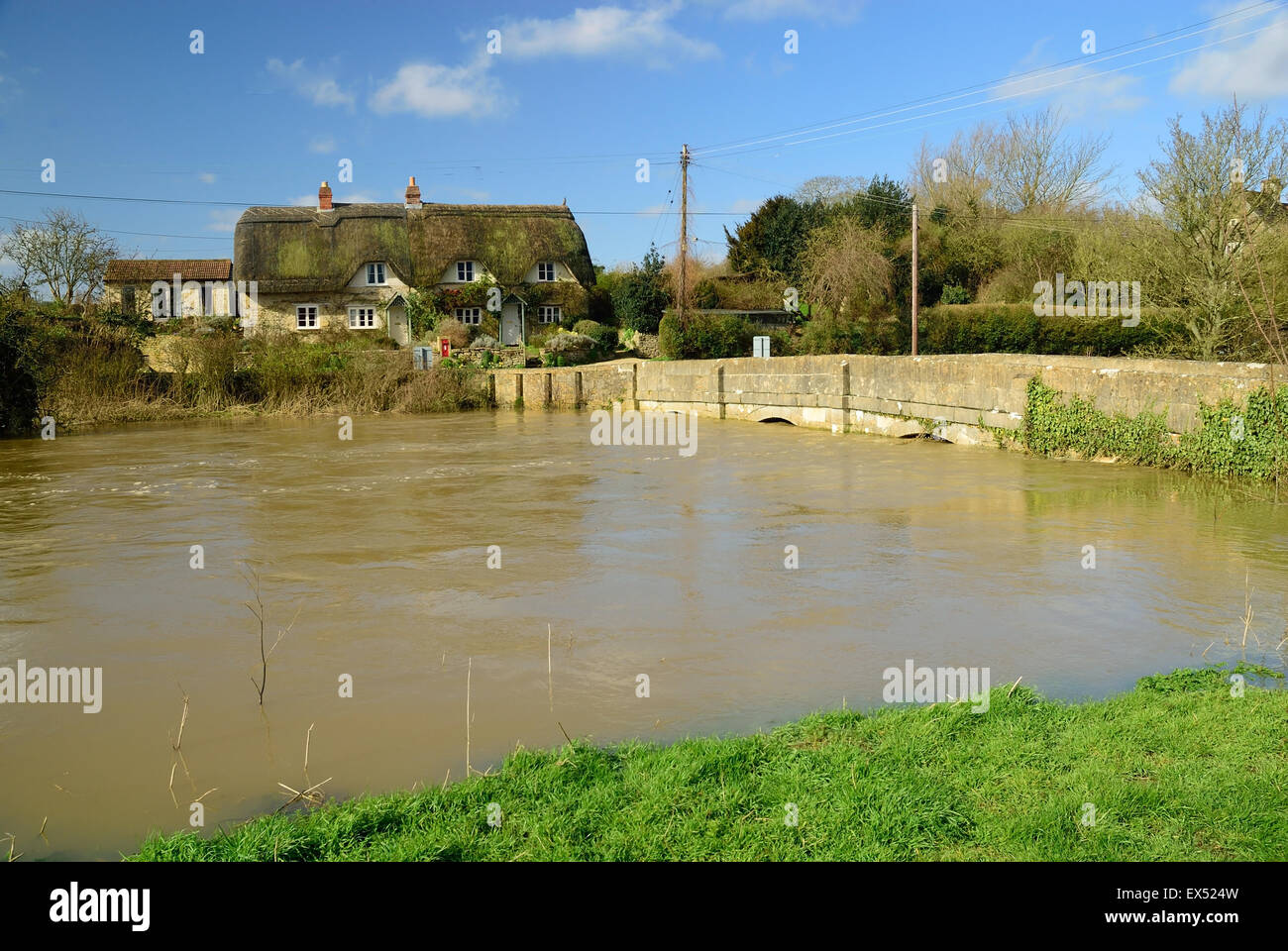 Cottage di paglia accanto al fiume gonfio Avon a Reybridge, vicino Lacock, Wiltshire. Foto Stock