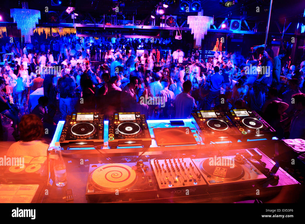 Immagine colorata di console di mixaggio e ponti per riprodurre musica e jolified clubbers in una discoteca sotto gli effetti di illuminazione fx in background Foto Stock