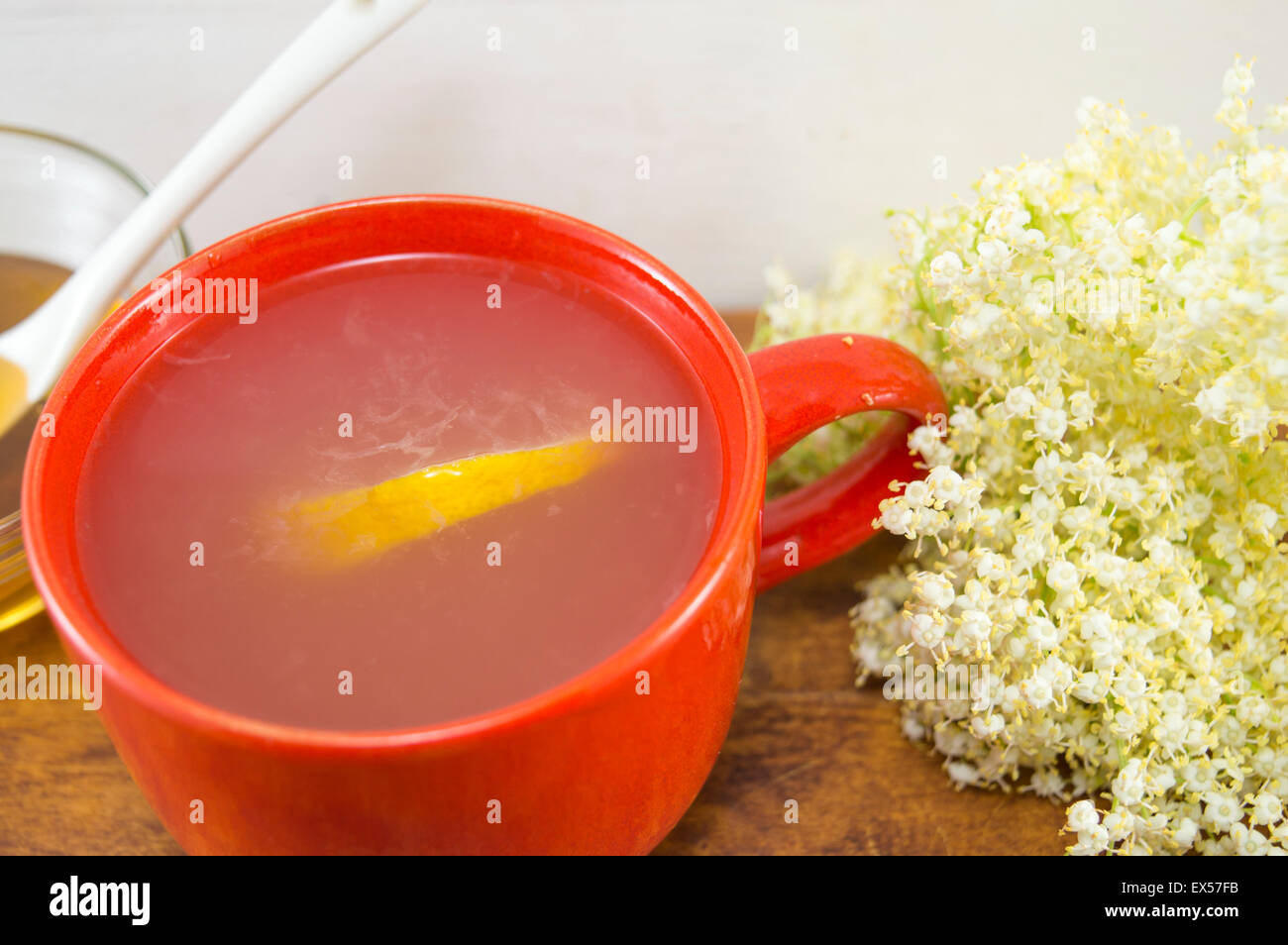 Anziano sano tè con limone servita con una ciotola di miele con un bilanciere su una tavola decorata con elderflowers Foto Stock