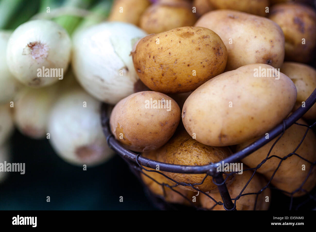 Le patate in un cesto in filo e cipolle Foto Stock