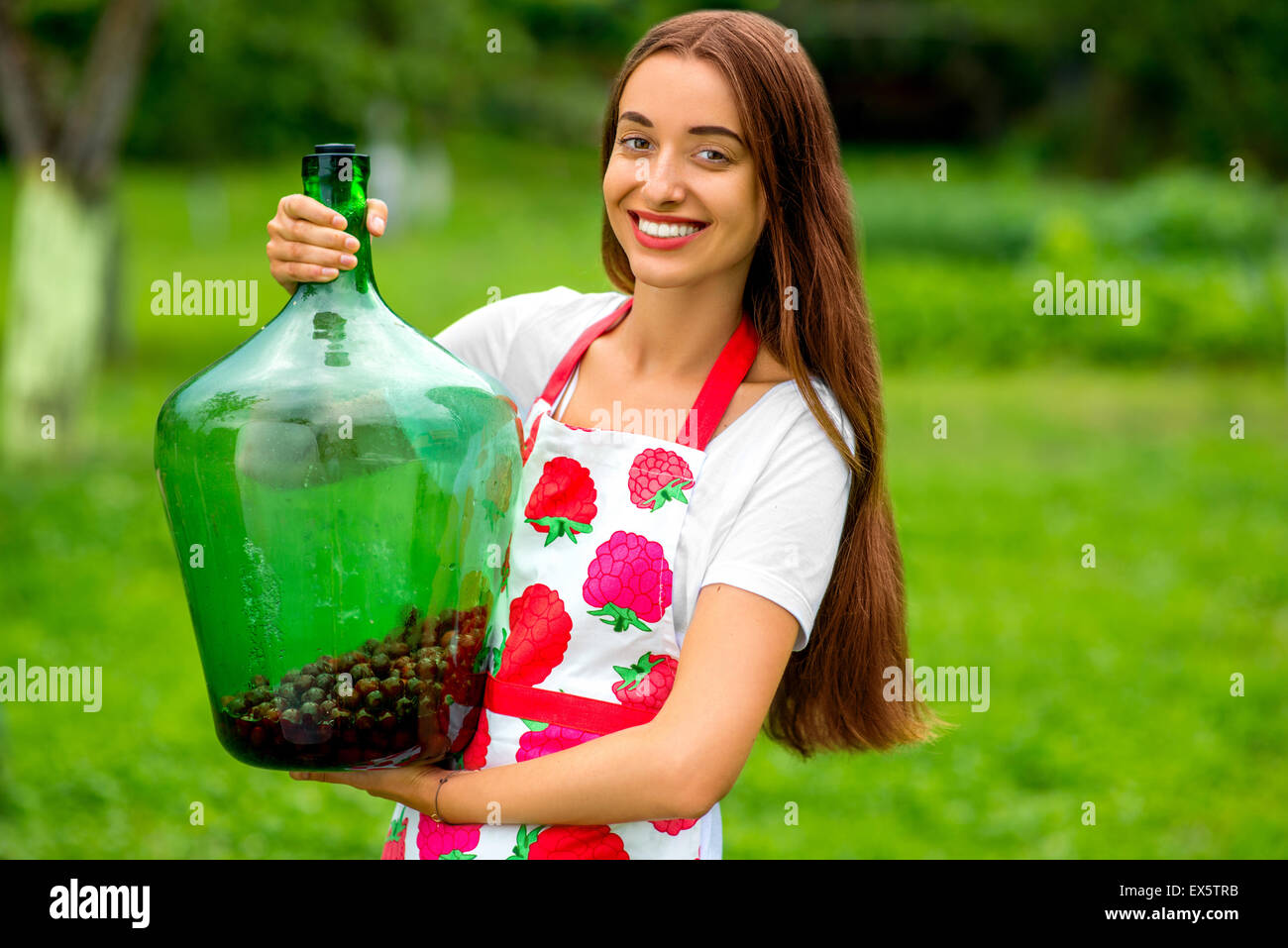 Donna che mantiene bottiglia grande con bacche rosse in giardino Foto Stock