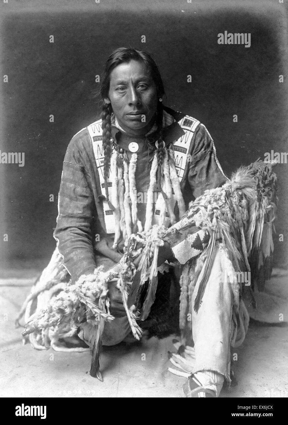 Nativi Americani, Piegan uomo, ritratto a figura intera, inginocchiata sul ginocchio destro, rivolto verso la parte anteriore, medicina di contenimento tubo. 1910; da Edward Curtis 1868-1952, fotografo Foto Stock