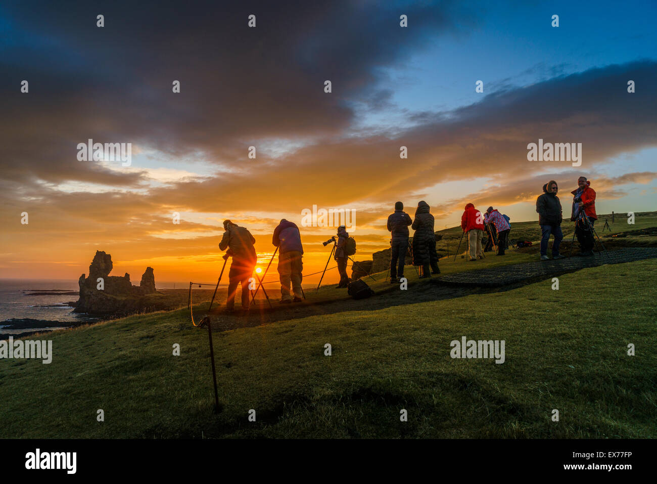 Il sole di mezzanotte e fotografi dal mare Londrangar pile e le scogliere Thufubjarg. Snaefellsnes Peninsula, Islanda Foto Stock