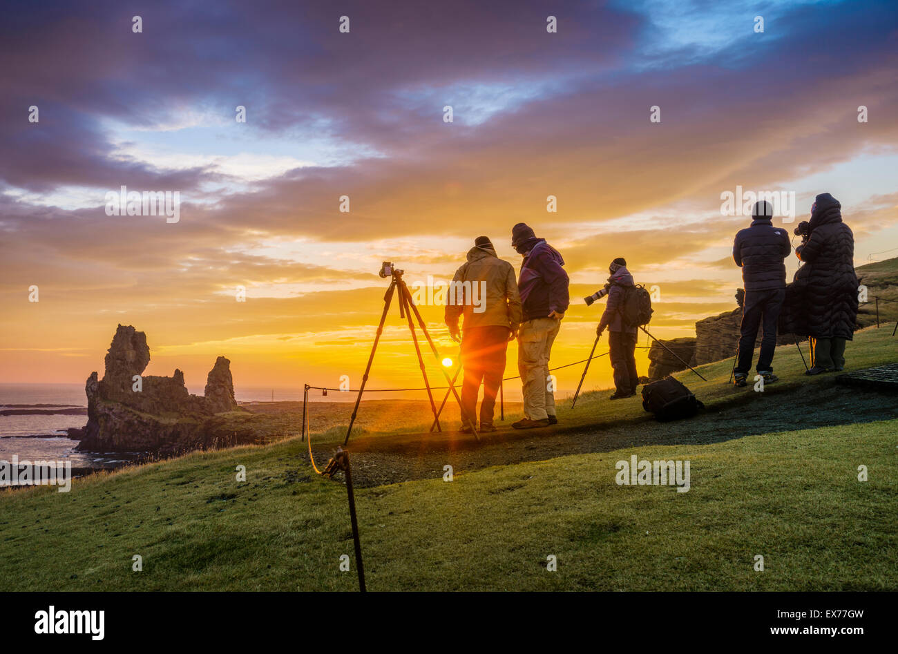 Il sole di mezzanotte e fotografi dal mare Londrangar pile e le scogliere Thufubjarg. Snaefellsnes Peninsula, Islanda Foto Stock