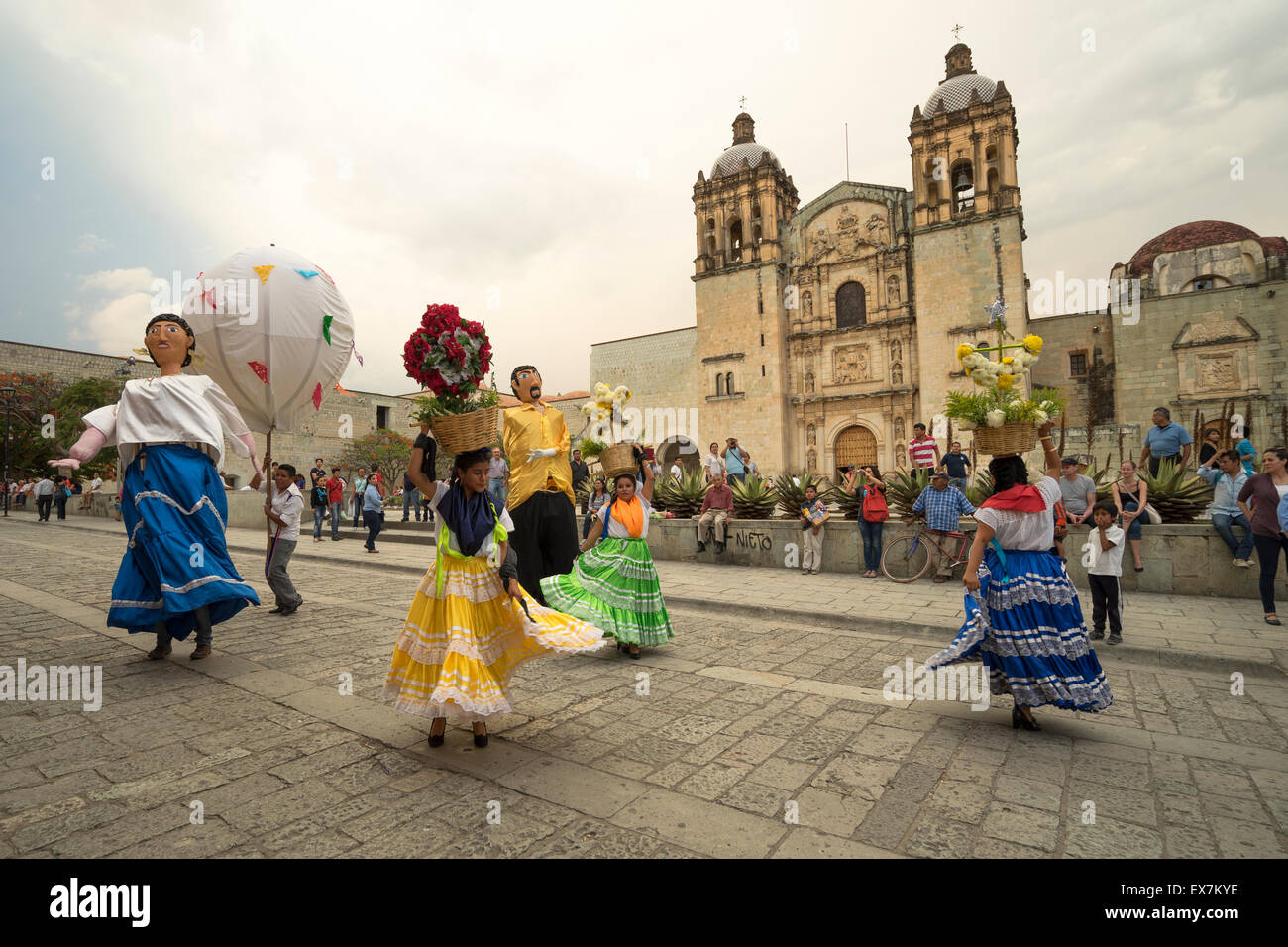 Le donne in costume e grandi figure danzanti nella parte anteriore della chiesa di Santo Domingo a una festa tradizionale in Messico Oaxaca Foto Stock