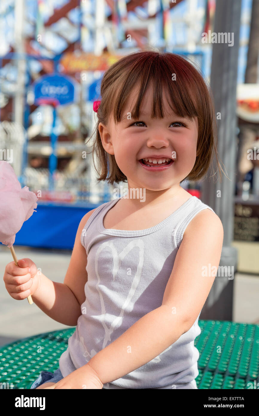 Bimba di tre anni di mangiare il cotone candy presso il parco di divertimenti, San Diego, California Foto Stock
