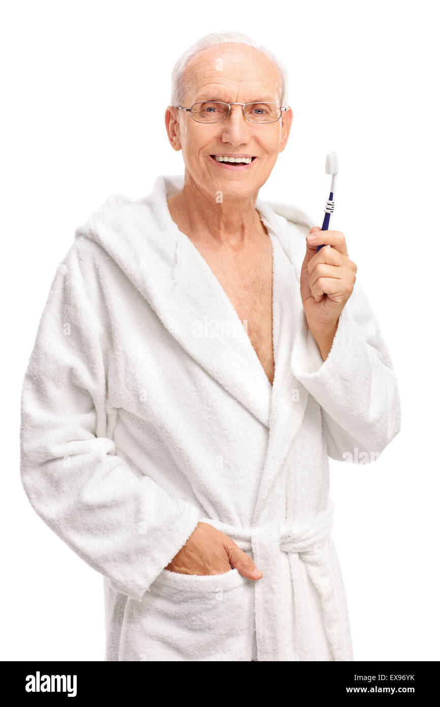 Colpo verticale di un allegro senior in un accappatoio tenendo uno spazzolino da denti e guardando la telecamera isolata su sfondo bianco Foto Stock