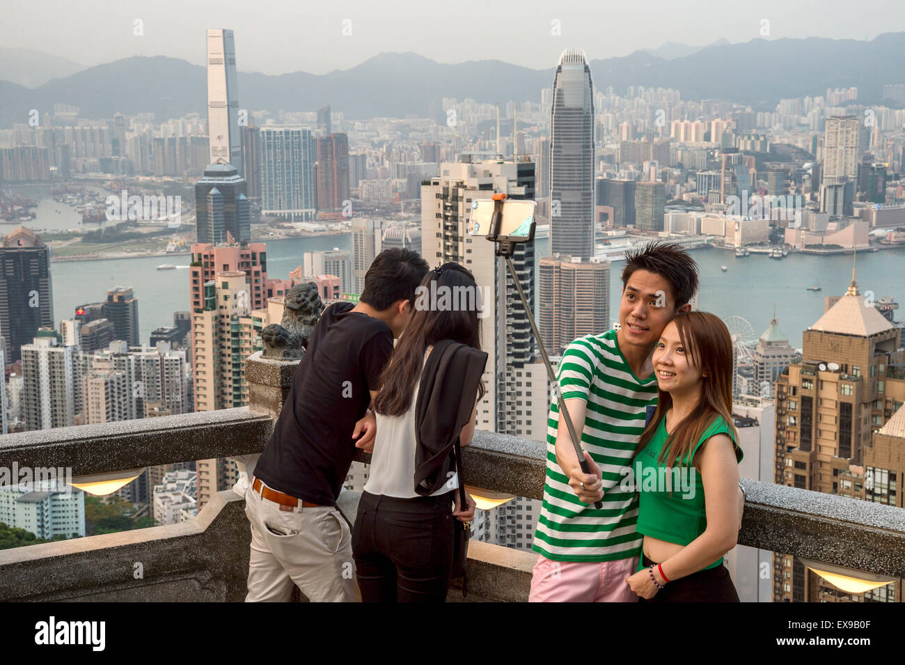 Giovani asiatici giovane usando un bastone selfie nella parte anteriore della skyline di Hong Kong, dal Victoria Peak Foto Stock