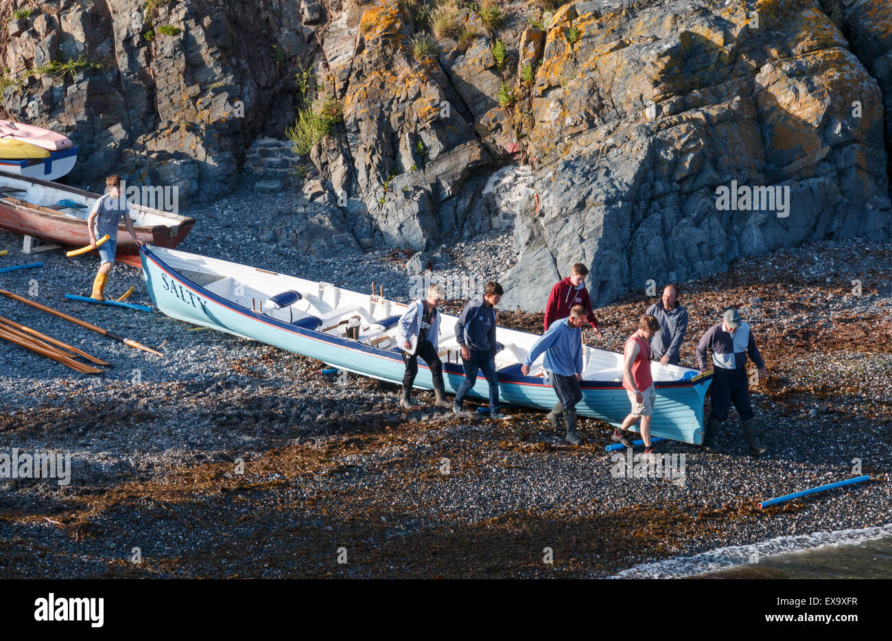 Gig racing - che porta la barca gid discesa a mare a Cadgwith Cove Cornovaglia Foto Stock