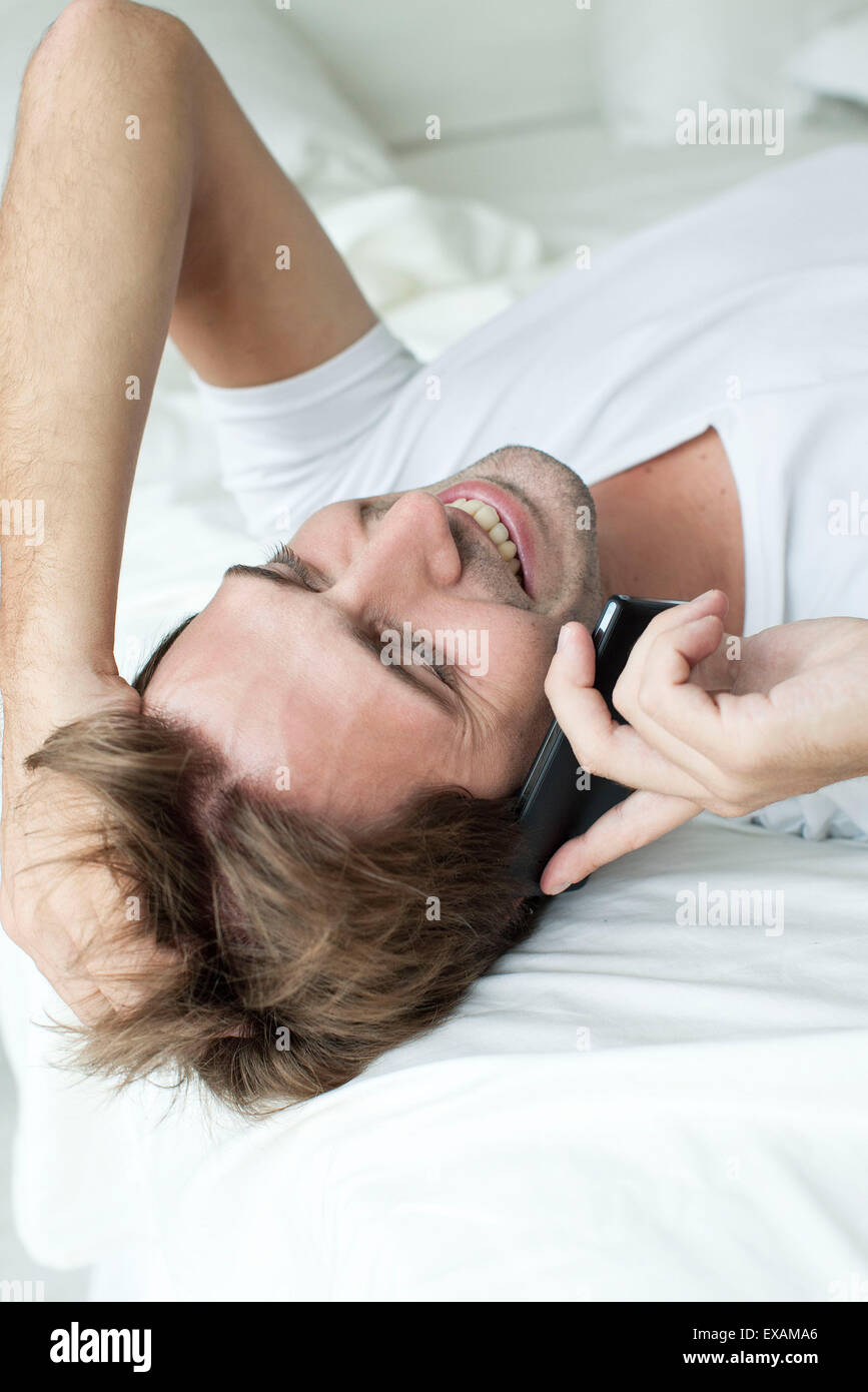 Uomo disteso sul letto, parlando al cellulare Foto Stock