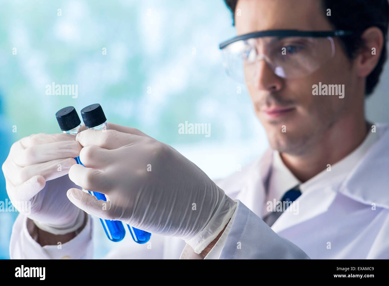 Scienziato scrutare le provette contenenti liquido blu in laboratorio Foto Stock