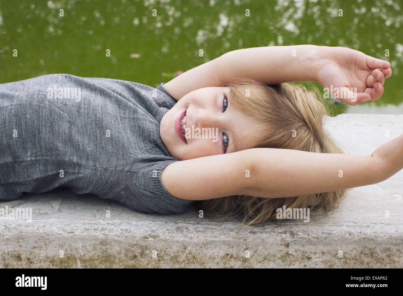 Bambina che giace accanto al laghetto, sorridente, ritratto Foto Stock