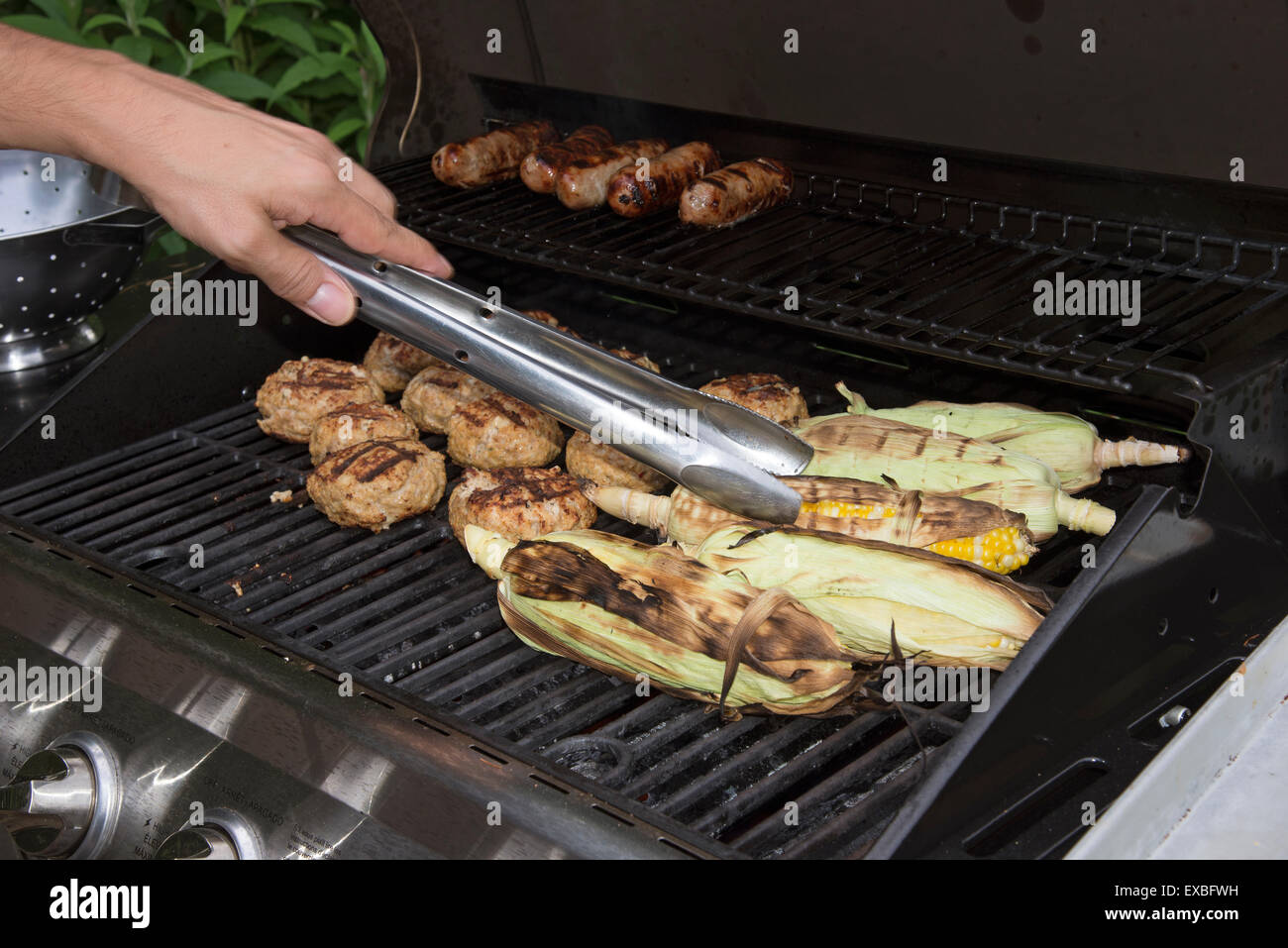 La cottura del cibo su un barbecue a gas. Salsicce, Turchia hamburger e il mais solo circa pronto a mangiare Foto Stock