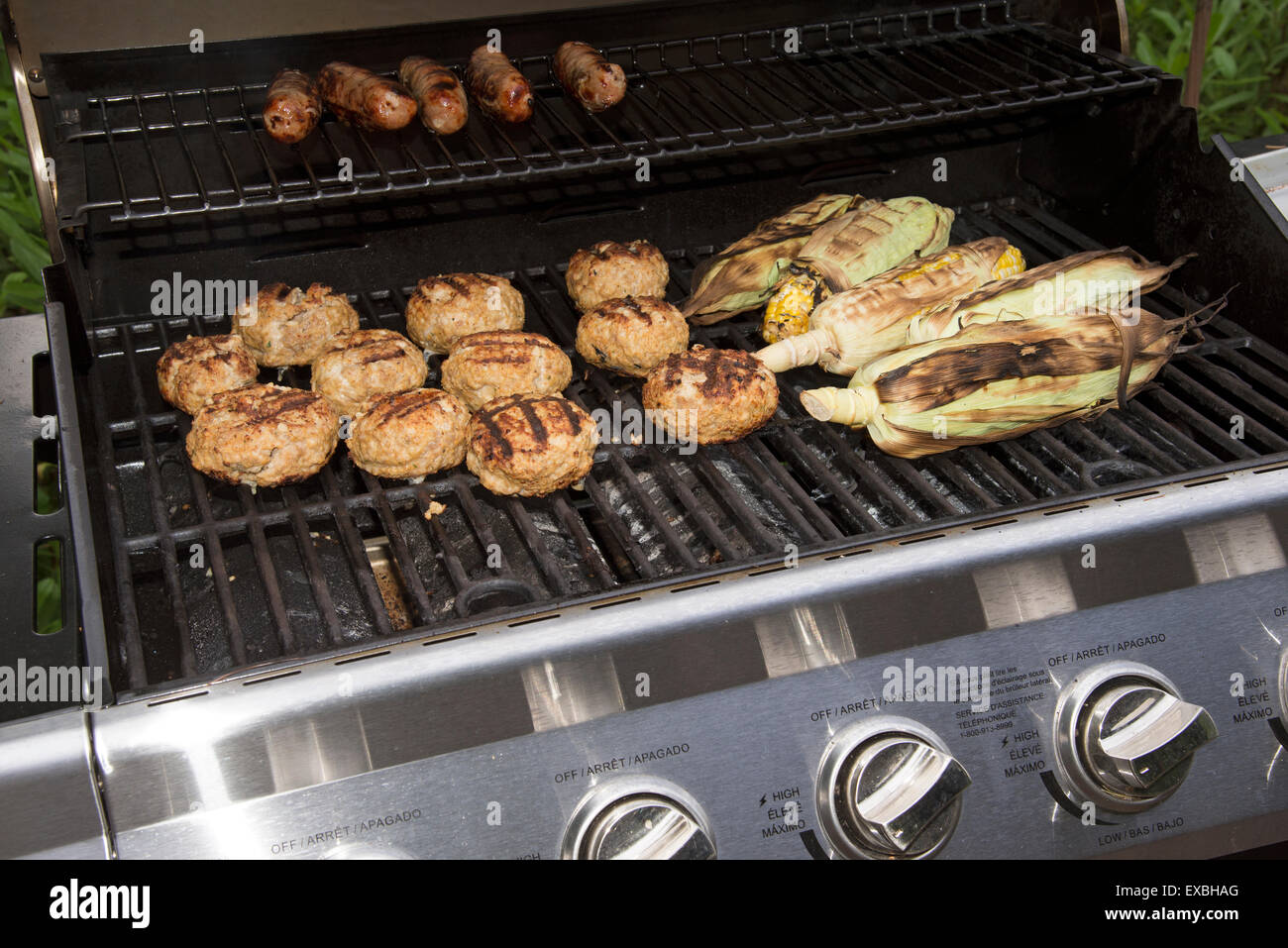 La cottura del cibo su un barbecue a gas. Salsicce, Turchia hamburger e il mais solo circa pronto a mangiare Foto Stock