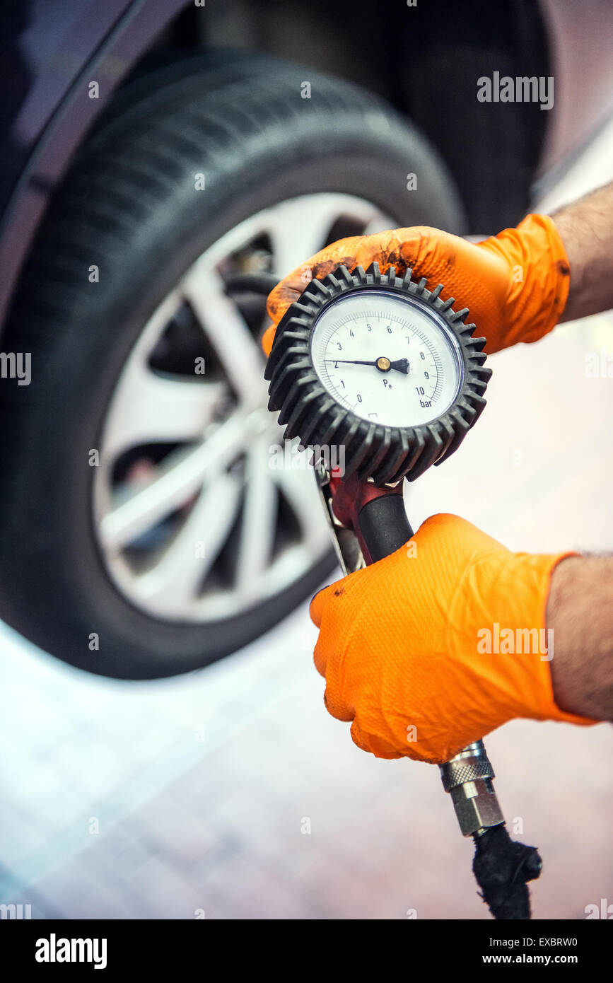Meccanico di controllo della pressione dei pneumatici tenendo un calibro collegato ad una pompa di aria nella sua mano come egli si inginocchia accanto alla ruota, chiudi Foto Stock