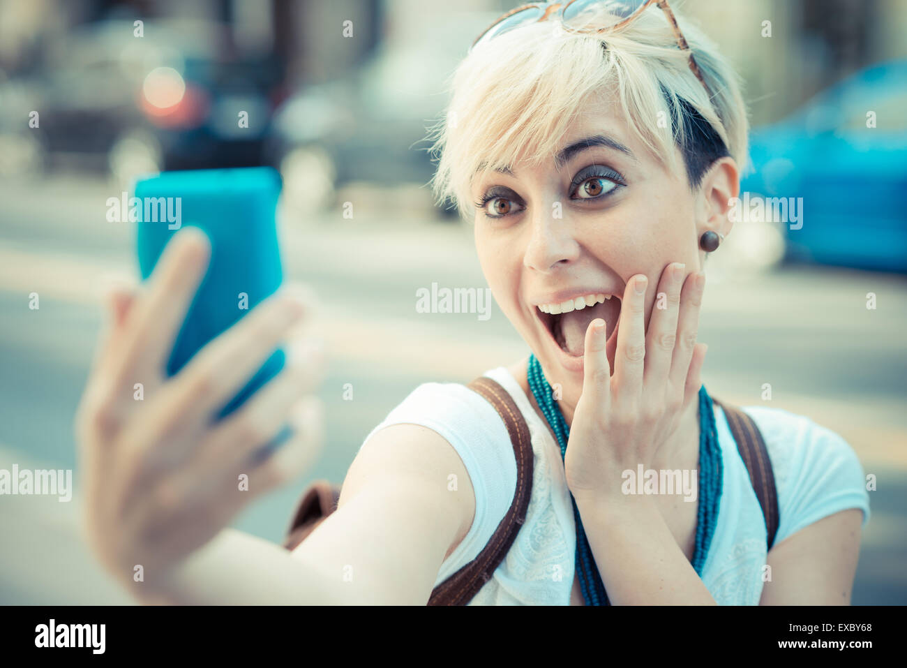 Giovane e bella bionda capelli corti hipster donna selfie nella città Foto Stock