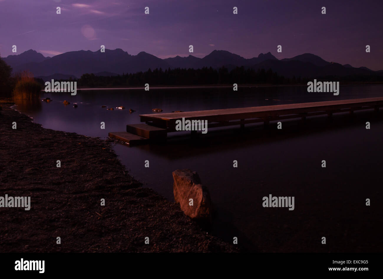 Lungo il molo su un lago di notte con montagne e foreste Foto Stock