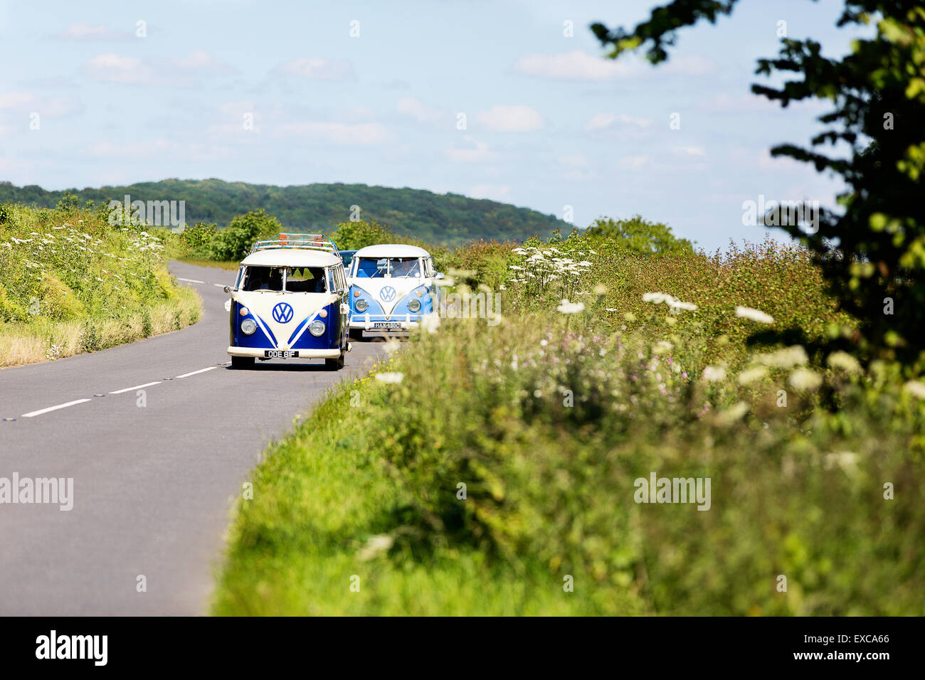 Due vecchi camper VW anni '1960 che guidano attraverso la campagna estiva inglese in convoglio Foto Stock