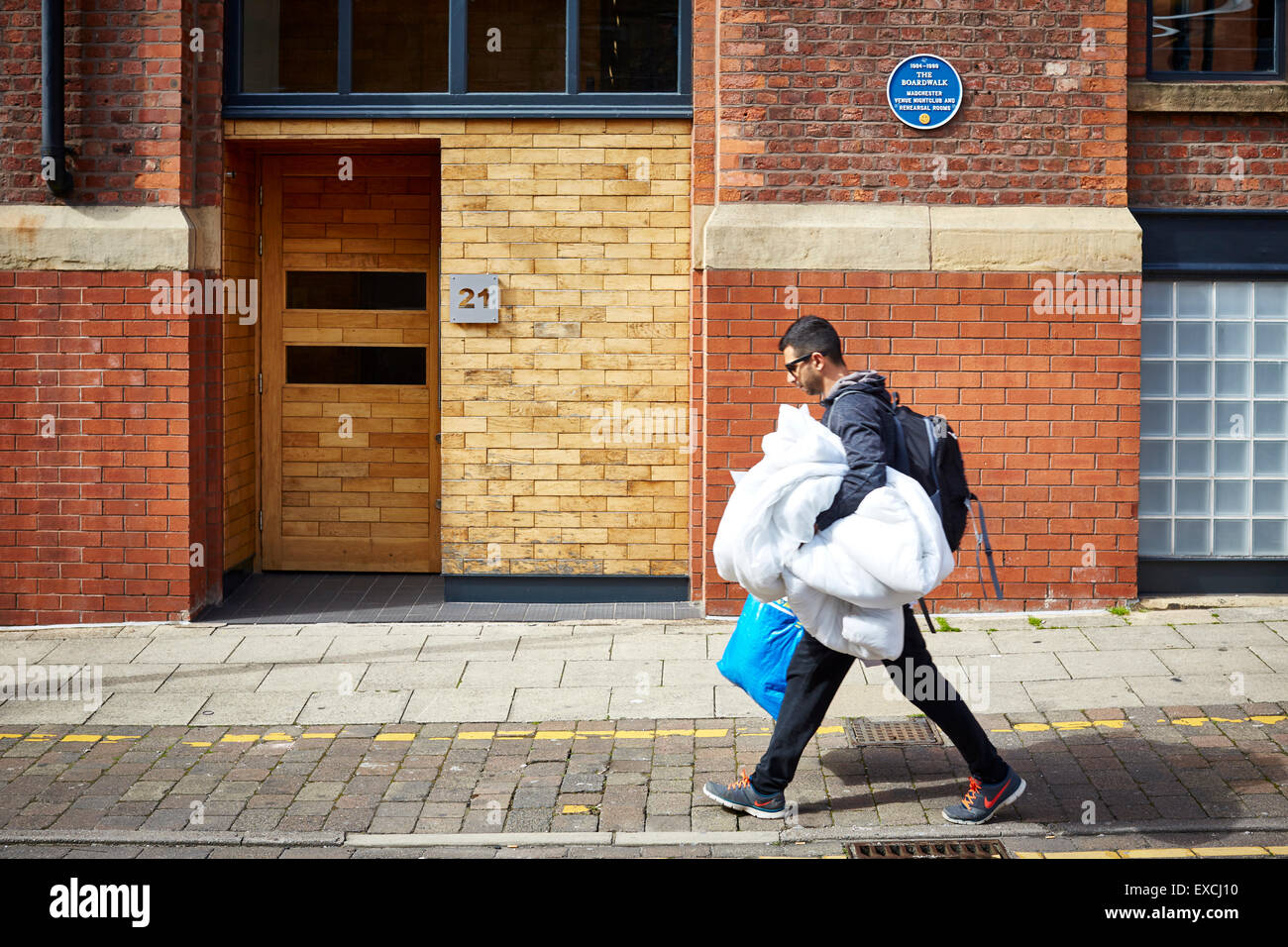 Il vecchio Boardwalk nightclub di Manchester Regno Unito un uomo passa portando il lavaggio Servizio lavanderia Lavaggio a secco Servizio fogli ikea borsa blu asian il Foto Stock