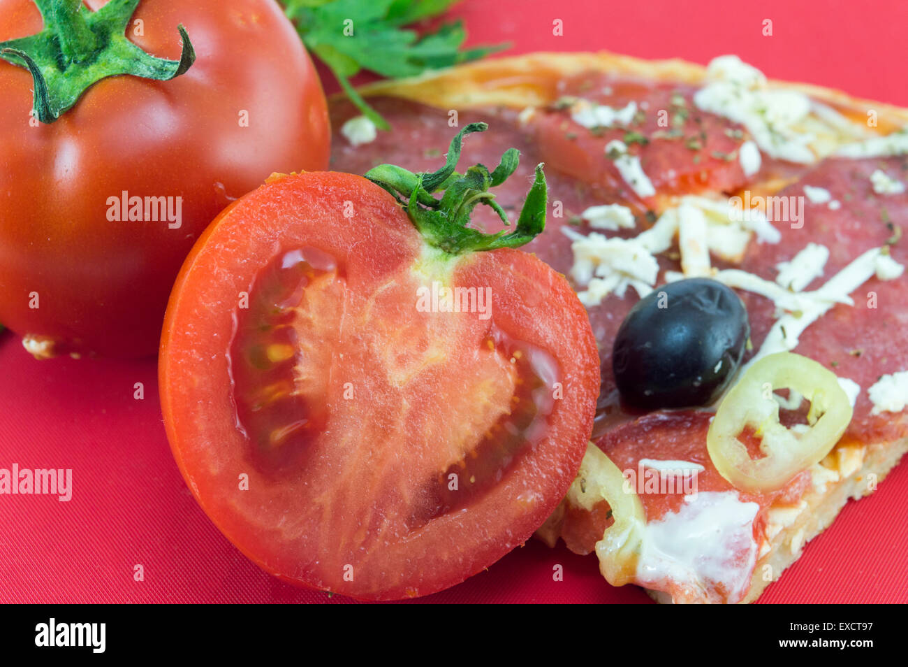 Dimezzato il pomodoro con un trancio di pizza e prezzemolo su sfondo rosso Foto Stock