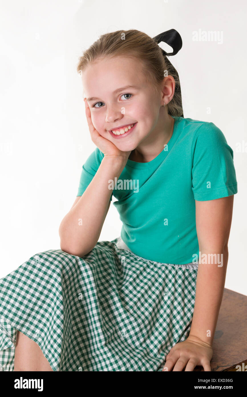 Giovane ragazza seduta con il viso appoggiato sulla mano di sorridere alla telecamera. Foto Stock