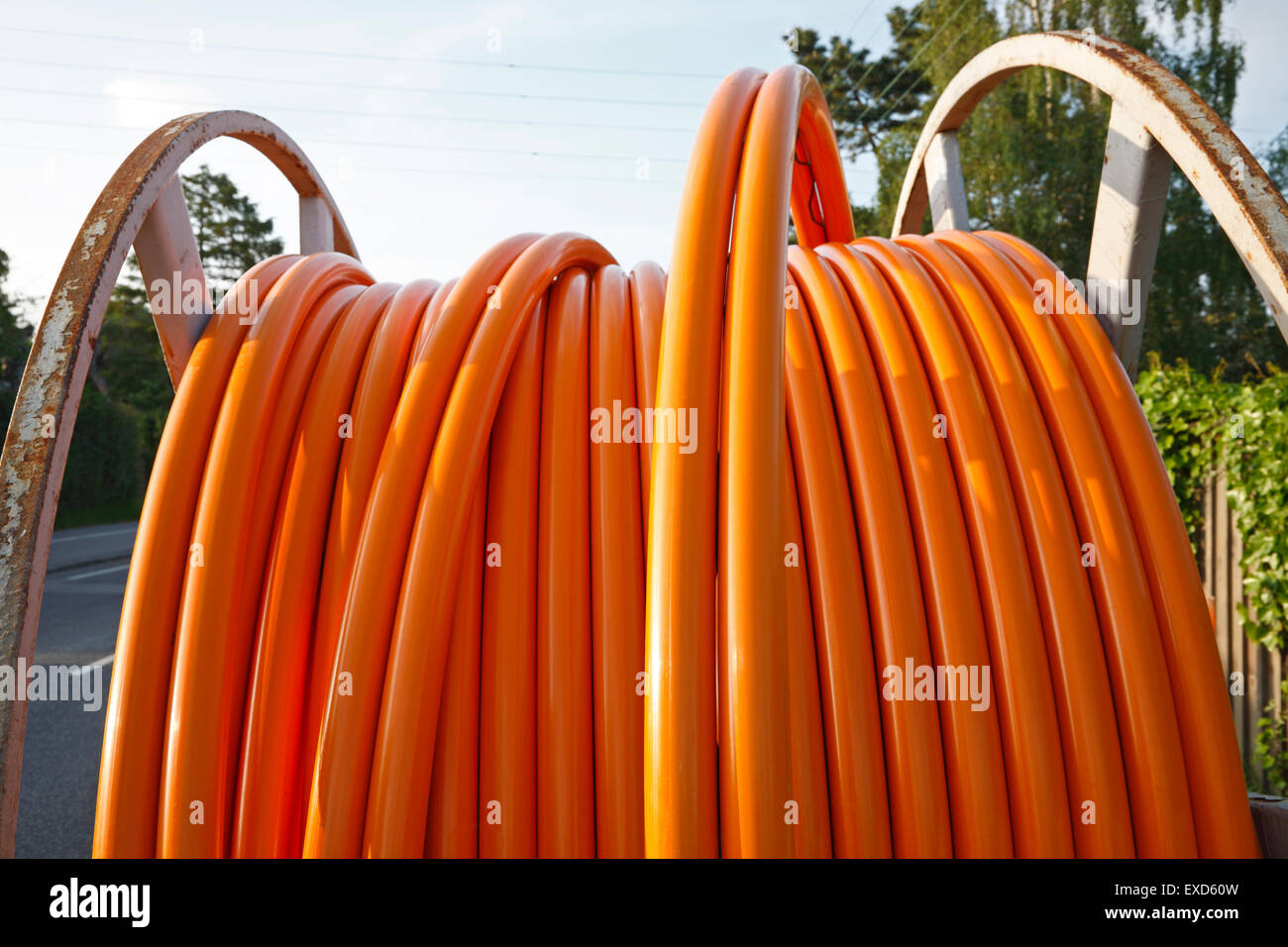 Il cavo arancione per le connessioni a banda larga su un rullo avvolgicavo in acciaio su una strada suburbana. Foto Stock Il cavo arancione per le connessioni a banda larga su un rullo avvolgicavo in acciaio su una strada suburbana. Foto Stock