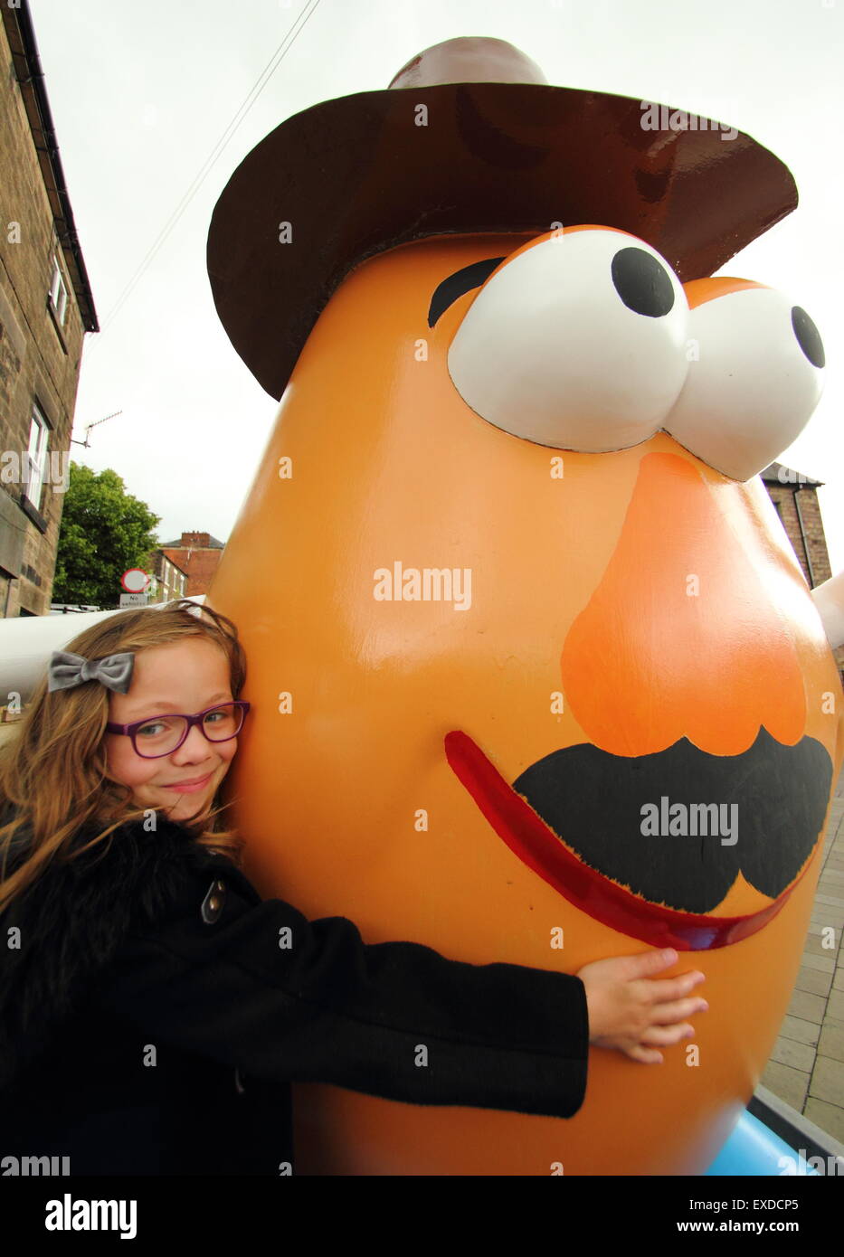 Belper, Derbyshire, Regno Unito. 12 Luglio, 2015. Brii Matheson, 8,da Belper abbracci un gigante Mr Potato Head che ha ri-apparve in Derbyshire città. La 7ft statua in fibra di vetro è stato regalato a Belper nel 2001 dalla sua città gemelle, Pawtucket, Rhode Island, Stati Uniti d'America. Dopo essere stato ribattezzato "onstrosity" da parte di alcuni locali, il carattere divisivo realizzati titoli nazionali. È stato soggetto ad atti vandalici e bandito. Ora il spud è stata spruced fino da un gruppo locale di giovani e svelato a Belper's Food festival di oggi. Credito: Deborah Vernon/Alamy Live News Foto Stock