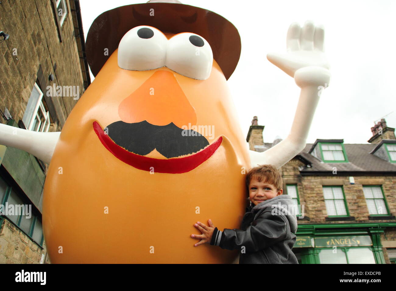 Belper, Derbyshire, Regno Unito. 12 Luglio, 2015. Tre-anno-vecchio Darwyn Reed da Belper abbracci un gigante Mr Potato Head che ha ri-apparve in Derbyshire città. La 7ft statua in fibra di vetro è stato regalato a Belper nel 2001 dalla sua città gemelle, Pawtucket, Rhode Island, Stati Uniti d'America. Dopo essere stato ribattezzato "onstrosity" da parte di alcuni locali, il carattere divisivo realizzati titoli nazionali. È stato soggetto ad atti vandalici e bandito. Ora il spud è stata spruced fino da un gruppo locale di giovani e svelato a Belper's Food festival di oggi. Credito: Deborah Vernon/Alamy Live News Foto Stock